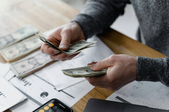 Close-Up Shot of a Person Holding Paper Money over printed out charts